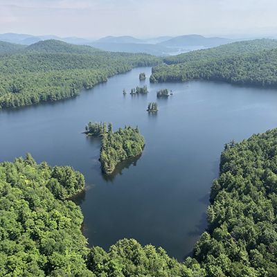 Aerial view of Jabe Pond. The pond is blue and surrounded by lush green forest.