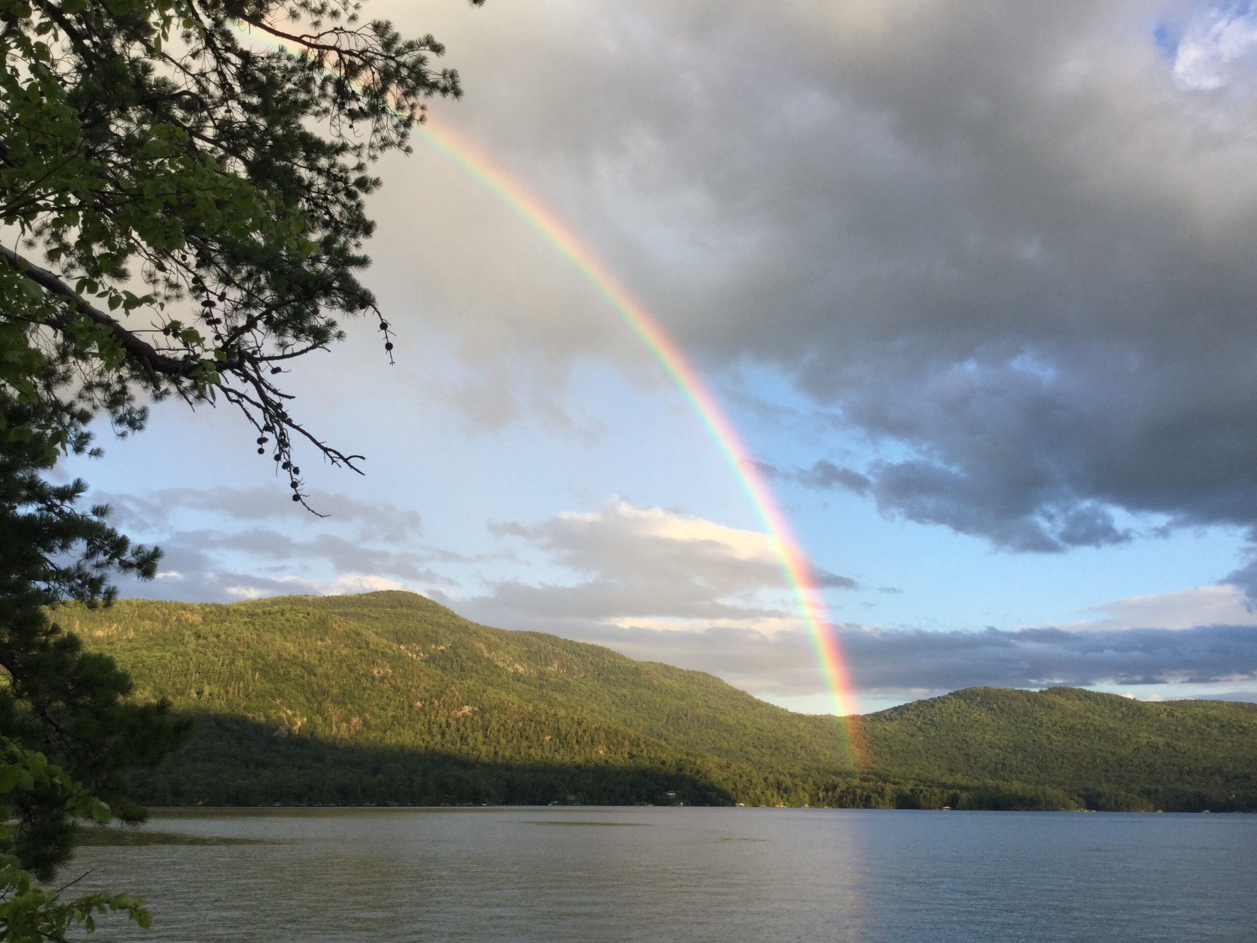 A rainbow can seen over a lake with lush green mountains in the background.
