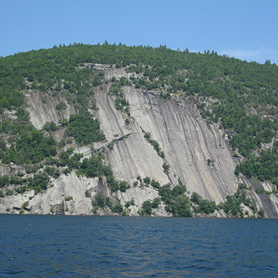 A dramatic rock cliff, its weathered surface etched with time, rises above a still lake nestled among trees.