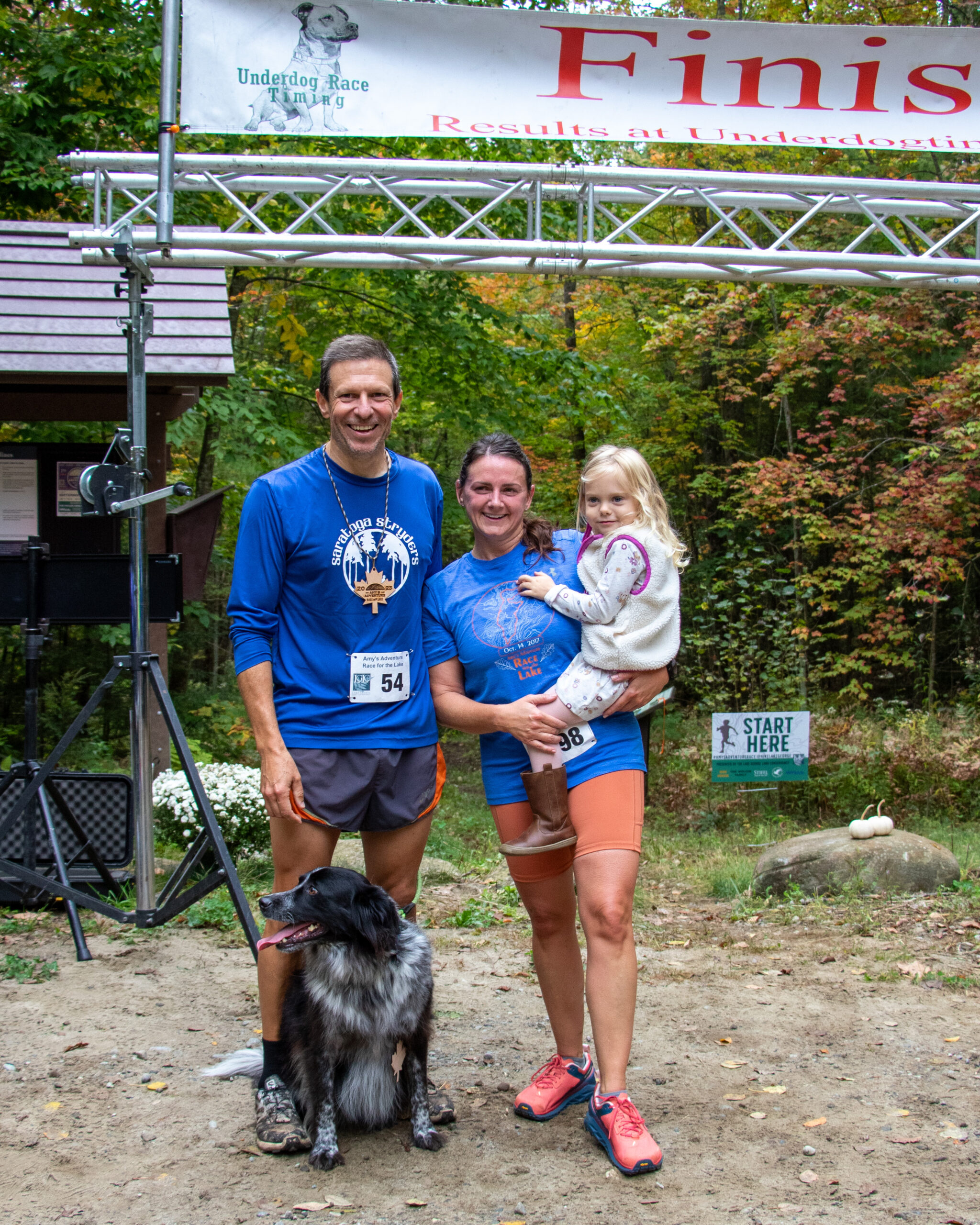 A family of three and their dog pose in front of the finish line.