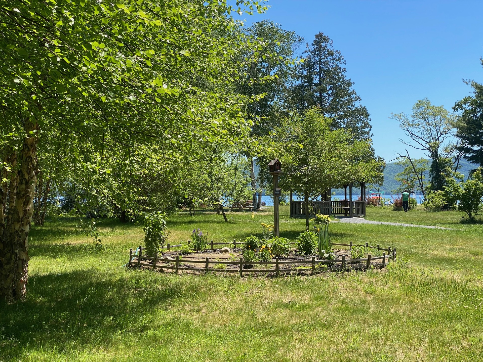 A garden and picturesque gazebo nestled amidst a park's greenery and lake in the background.