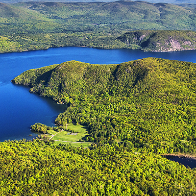 Aerial photo of Glenburnie showing the azure blue water of Lake George surrounded by green forested mountains. The wetlands and stream corridor of Sucker Brook are in the forefront. Photo by Carl Heilman, II/Wild Visions. Inc.