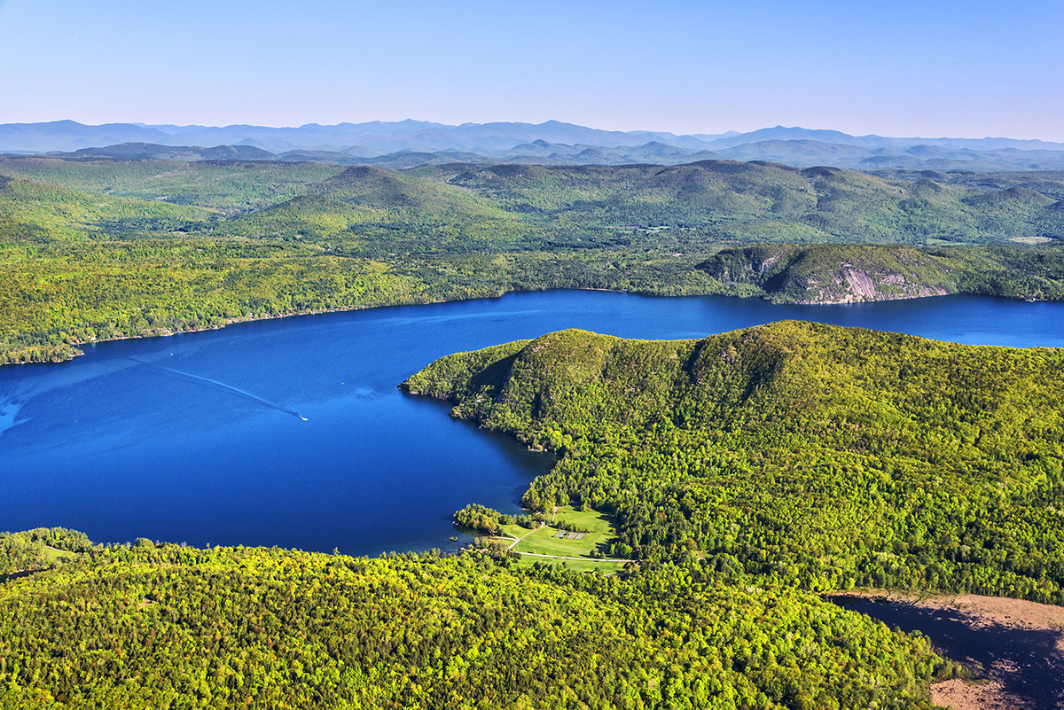 Photo by Carl Heilman, II/Wild Visions, Inc.. Bright green mountains are divided by the blue Lake George. The blue stream and wetlands of Sucker Brook are in the foreground, shown flowing into the lake.